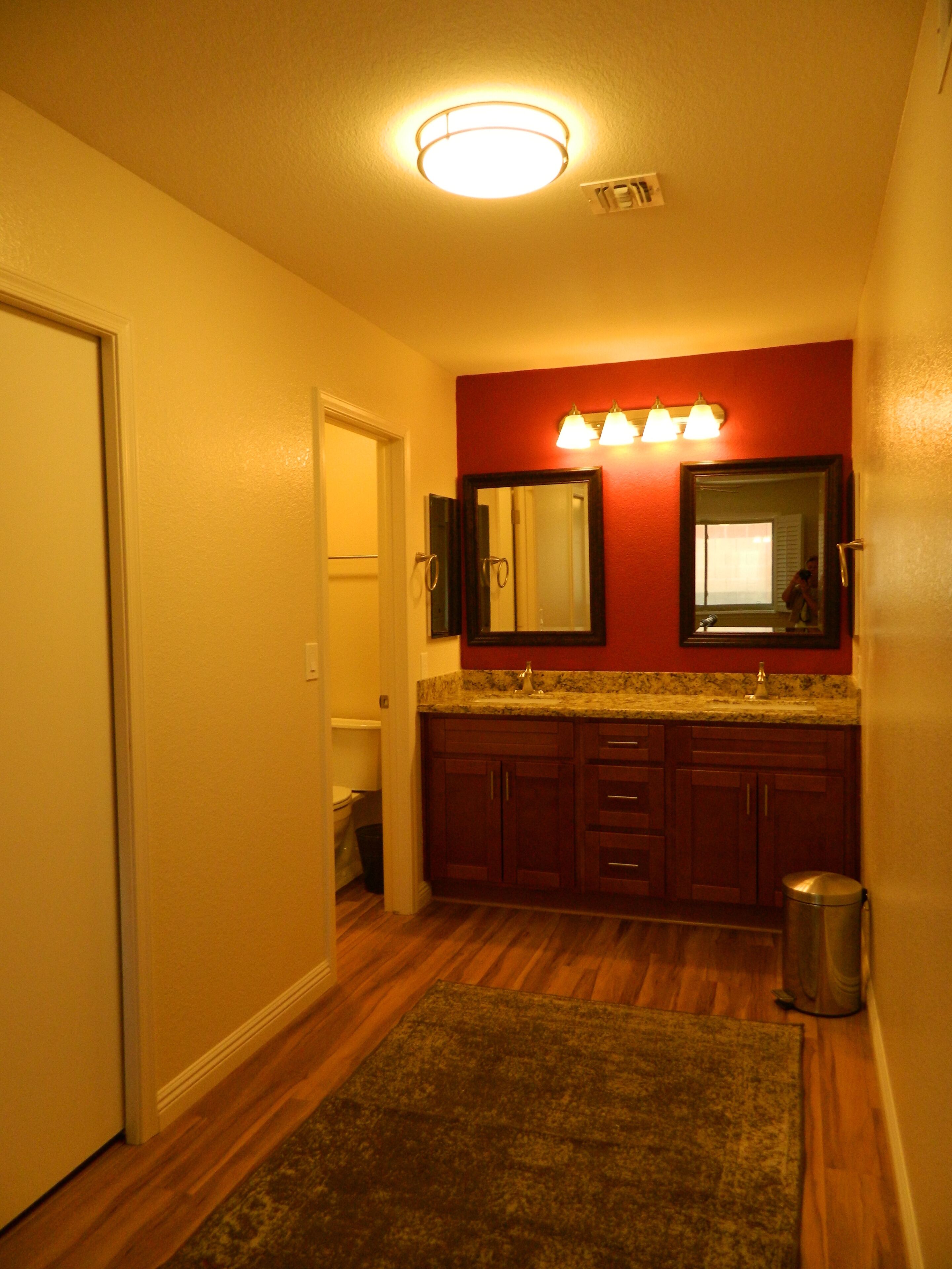 A bathroom with wooden flooring, a granite countertop, and a red accent wall.