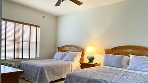 A bedroom with two beds, a nightstand with a lamp, a ceiling fan, and a window with blinds. - Condo in Legends Golf Course Resort  with a great Pub Next Door to the Unit (Myrtle Beach)