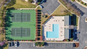 An aerial view of a property with two tennis courts, a swimming pool, and a parking lot.
