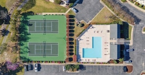 An aerial view of a property with two tennis courts, a swimming pool, and a parking lot.
