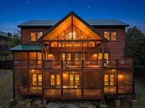 Une cabane en rondins à deux étages, dotée d’un balcon, de grandes fenêtres et d’un luminaire central.
