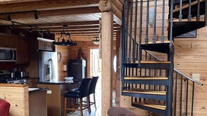 Interior acogedor de una cabaña con una escalera de madera, un comedor y una silla roja.
