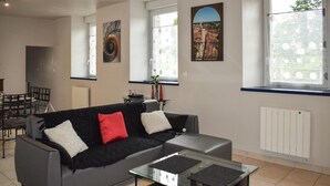 A modern living room with a grey sofa, a glass coffee table, and a dining area with a glass table and chairs. - 2 bedroom awesome home in Brélidy (Brélidy)