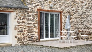 A stone building with a wooden door and a glass door, outdoor seating with metal chairs, and a small table. - 2 bedroom awesome home in Brélidy (Brélidy)