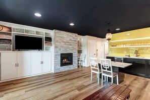 Una sala de estar moderna con chimenea, armarios blancos, un televisor y una zona de comedor con sillas.