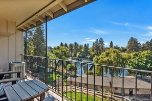 A balcony with a view of a river, trees, and a building in the background. - Top Floor Riverfront Condo at the edge of Downtown (Bend)