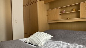 Una cama con una colcha estampada y una sola almohada, un armario de madera y una estantería con adornos.
