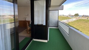 Un balcón con alfombra verde, un mueble de madera, una silla y vistas a un área con césped y edificios.