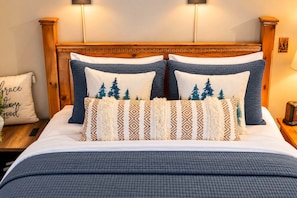 A bed with a wooden headboard, multiple pillows, and a bedside table with a lamp.