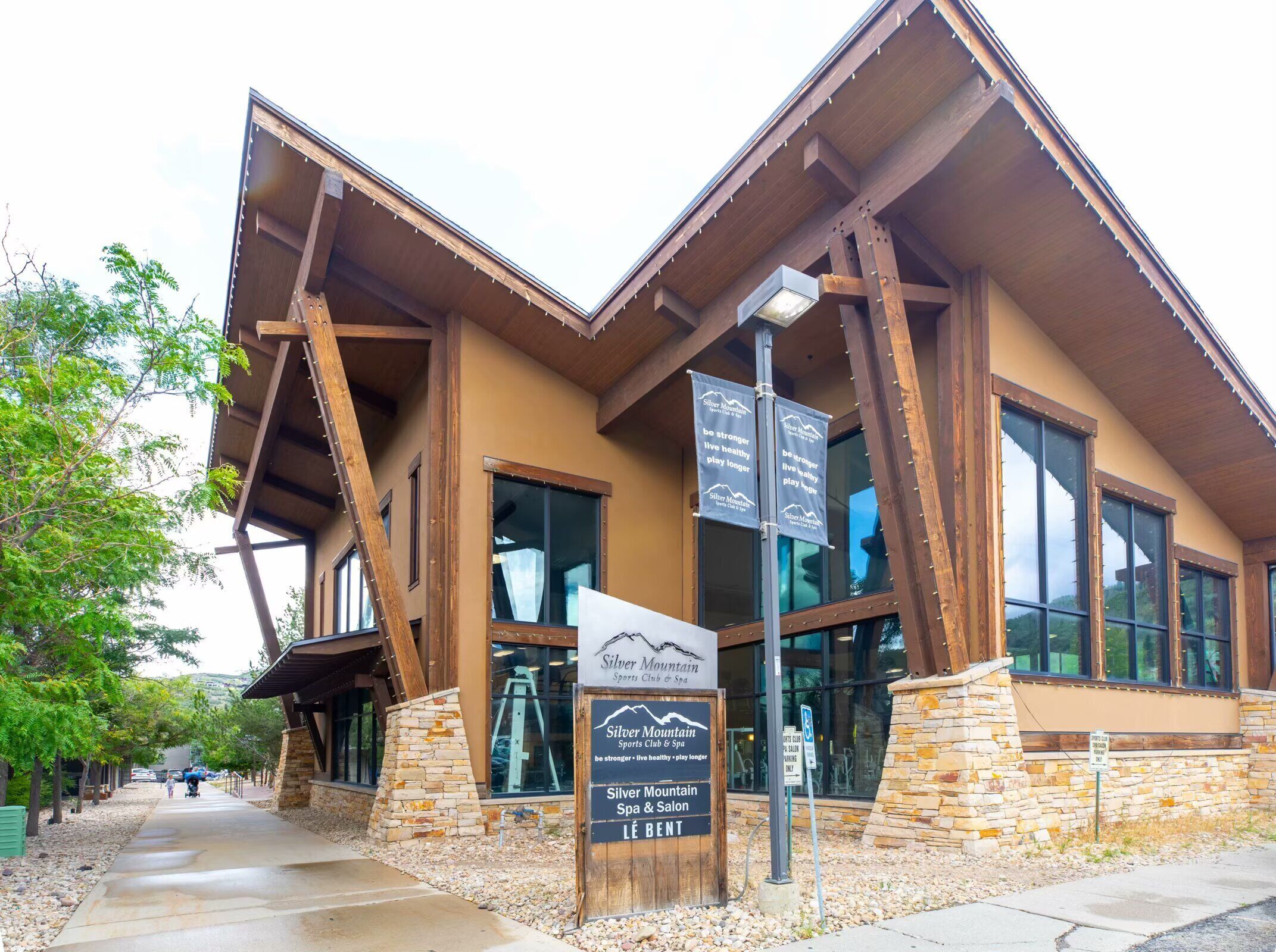 A building with a stone base and wooden beams, featuring large windows and a sign for Silver Mountain Sports Club & Spa.