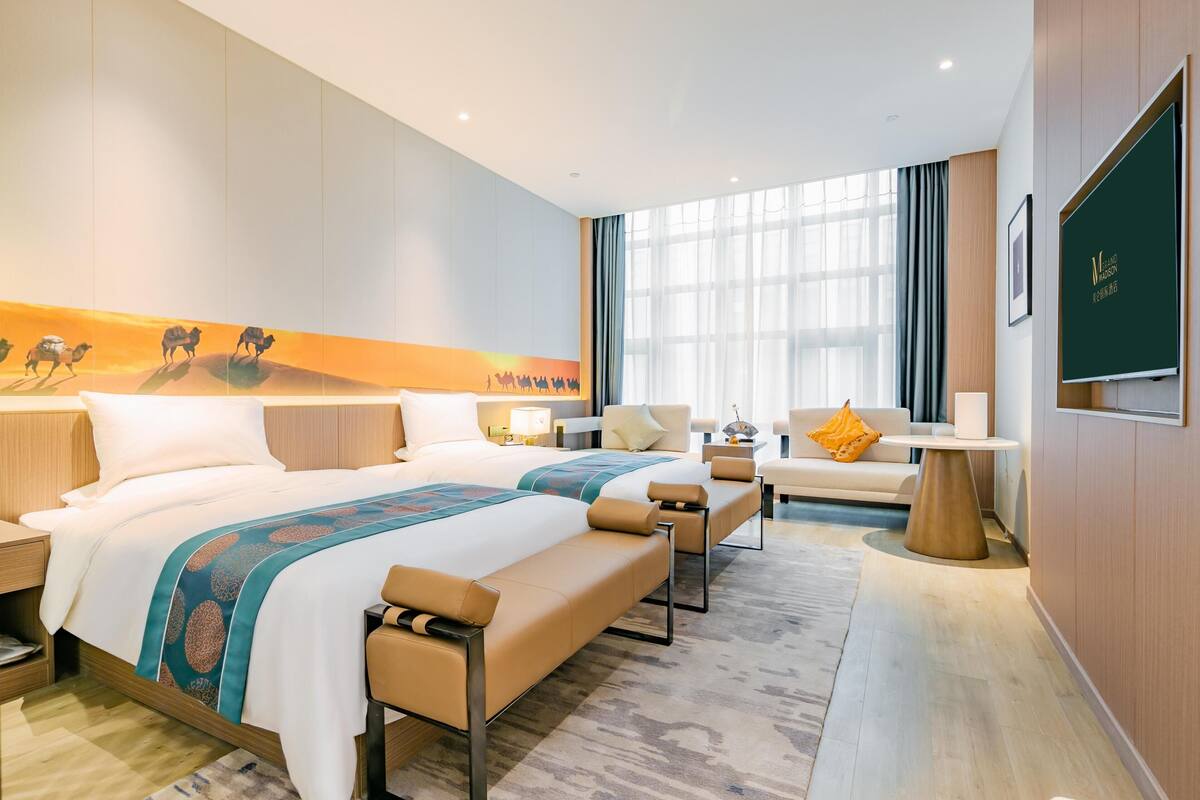 Ein Hotelzimmer mit einem großen Bett, einer Couch, einem kleinen Tisch und einem an der Wand befestigten Fernseher.