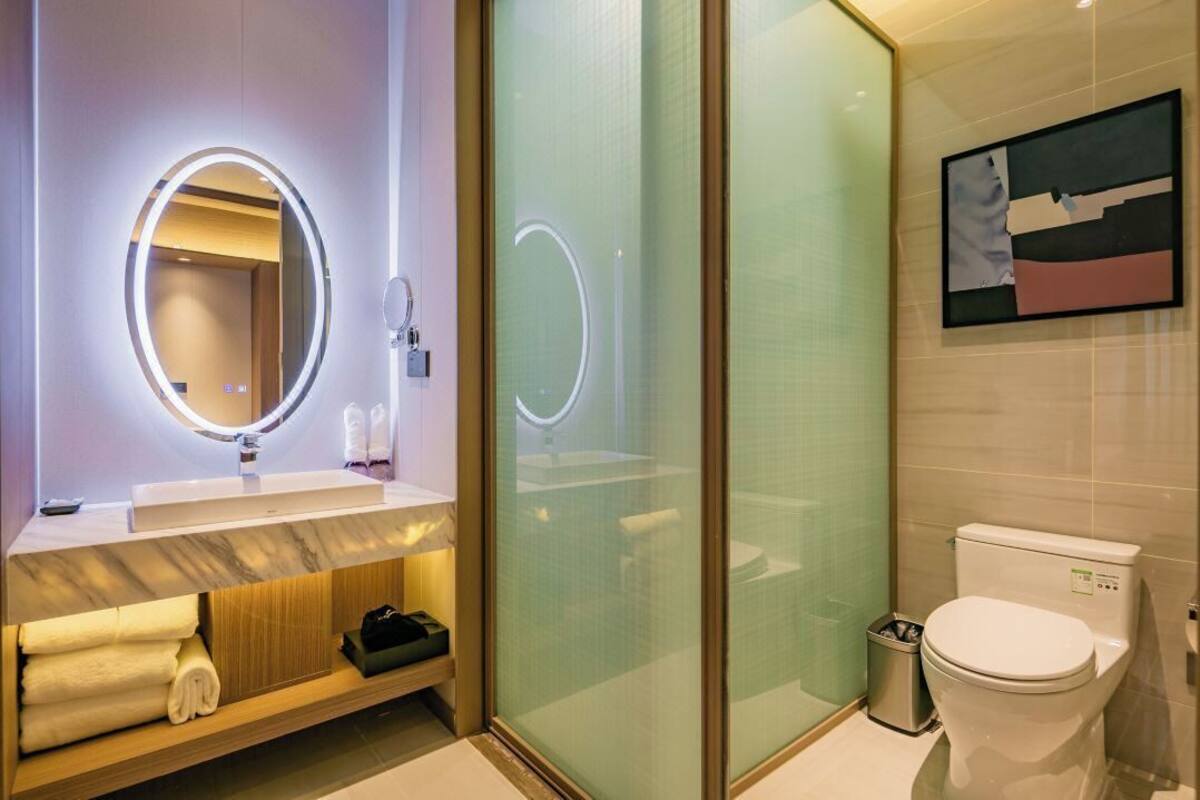 Ein modernes Badezimmer mit einem runden Spiegel, einer Toilette und einer Duschkabine aus Glas.
