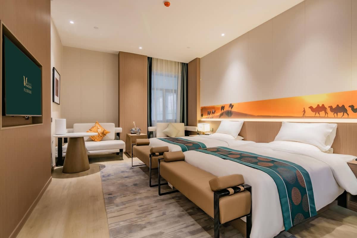 A hotel room with a large bed, two bedside tables, a sofa, a desk, and a wall-mounted TV.