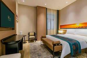 A hotel room with a bed, a desk, a chair, a window with curtains, and a wall-mounted TV.