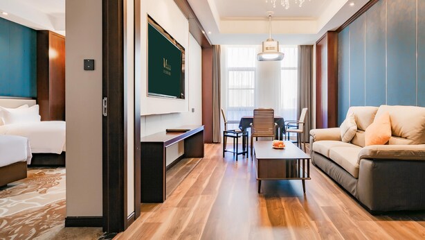 A hotel room with a bed, a desk, a sofa, a dining table with chairs, and a chandelier. - Grand Madison Xuchang Beihai (Xuchang)