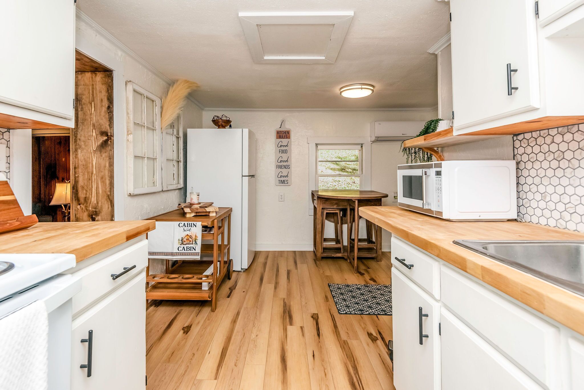 Una cocina compacta con suelo de madera, armarios blancos, un microondas y un pequeño comedor con mesa y sillas.