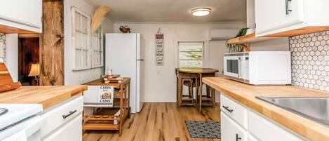 Una cocina compacta con suelo de madera, armarios blancos, un microondas y un pequeño comedor con mesa y sillas.