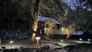 A rustic cabin with a wooden deck, surrounded by trees and a rocky path. - Cozy Mountain Cabin w/ hot tub and fire pit (Boone)