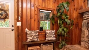 A wooden interior with a bench, two pillows, a potted plant, and a stone fireplace. - Cozy Mountain Cabin w/ hot tub and fire pit (Boone)