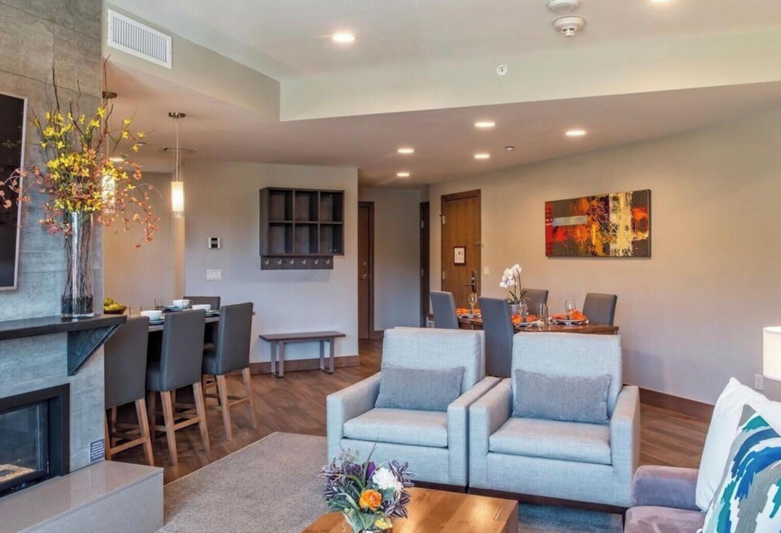 Uma sala de estar moderna com lareira, sofás cinzas, uma mesa de centro e um espaço de jantar com um banco.