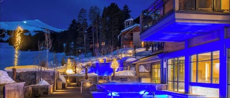 Un hotel moderno con zona de piscina, iluminada con luces azules, rodeado de paisaje nevado y árboles.