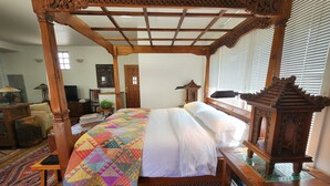 Un letto a baldacchino con una coperta colorata, un comodino in legno, una lampada e un armadietto in legno tradizionale.