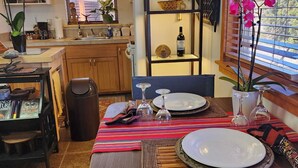 Zona pranzo con tavolo apparecchiato per due, cucina sullo sfondo e oggetti decorativi sugli scaffali.