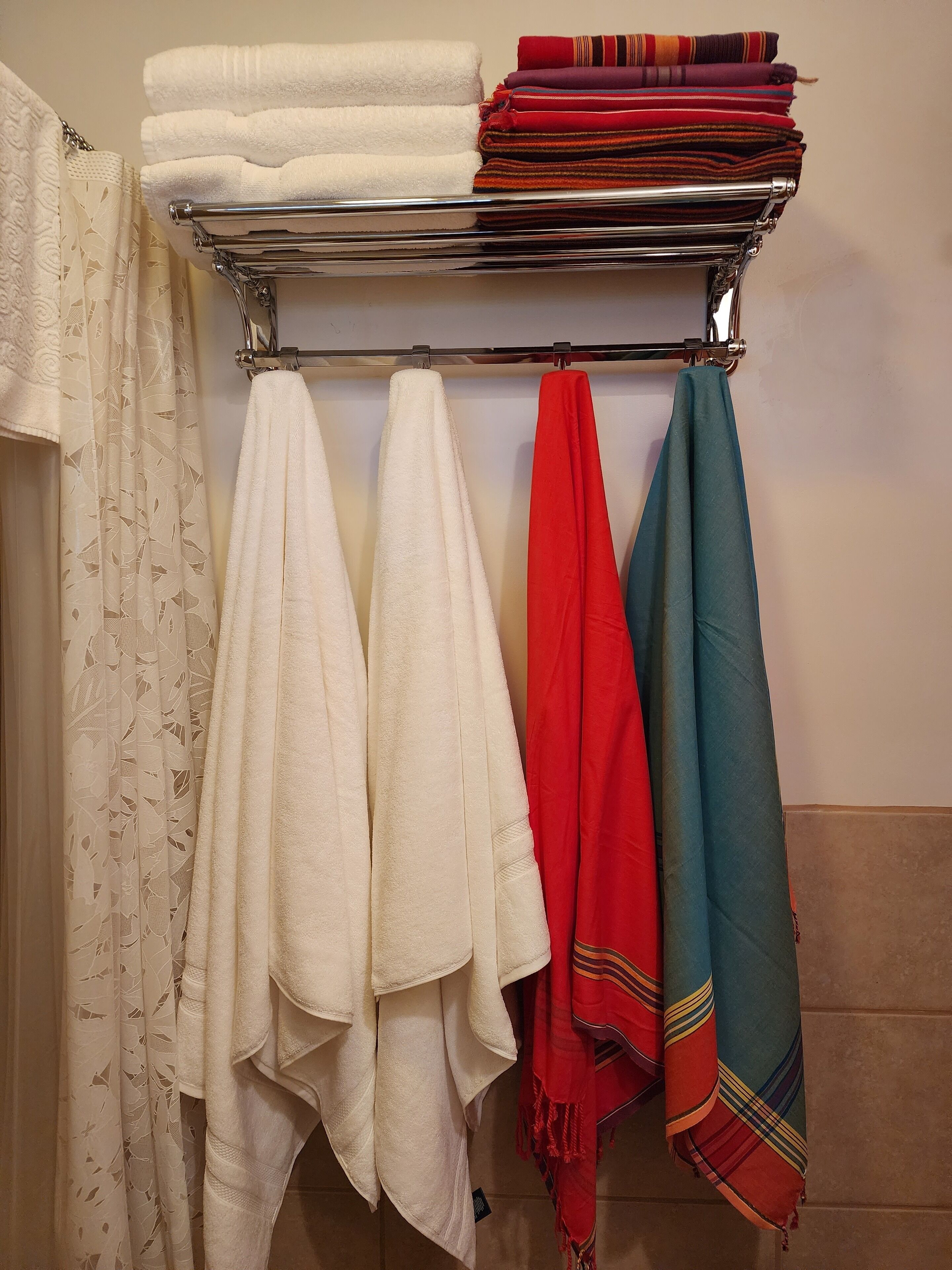 A bathroom with a towel rack holding several towels and a folded blanket.