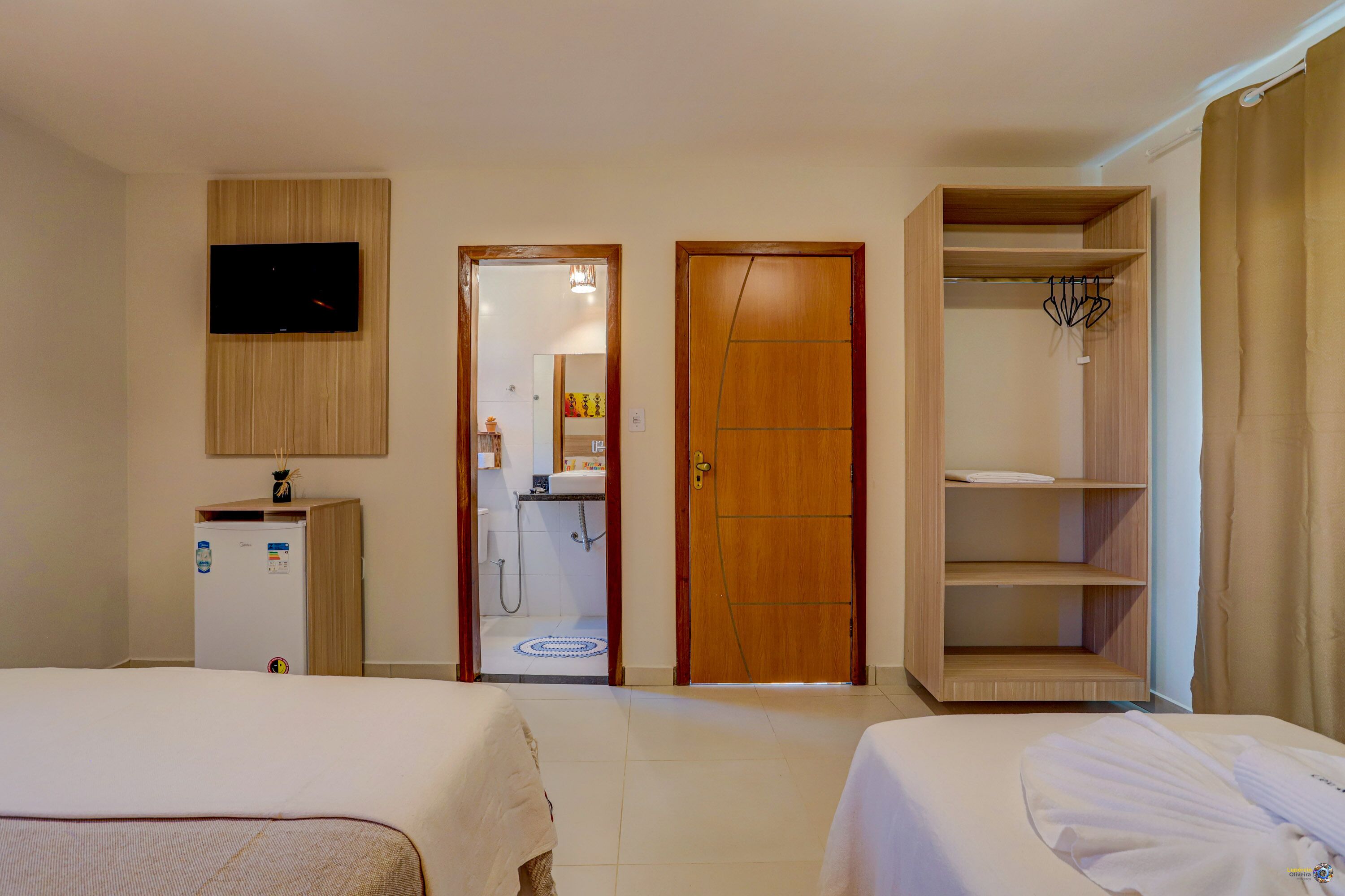 Habitación de hotel con dos camas, televisión, armario y baño visible a través de una puerta abierta.