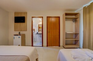 Habitación de hotel con dos camas, televisión, armario y baño visible a través de una puerta abierta.