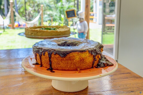 A cake on a white cake stand with a chocolate glaze dripping down the sides. - Pousada Céu & Mar de Taipu (Maraú)