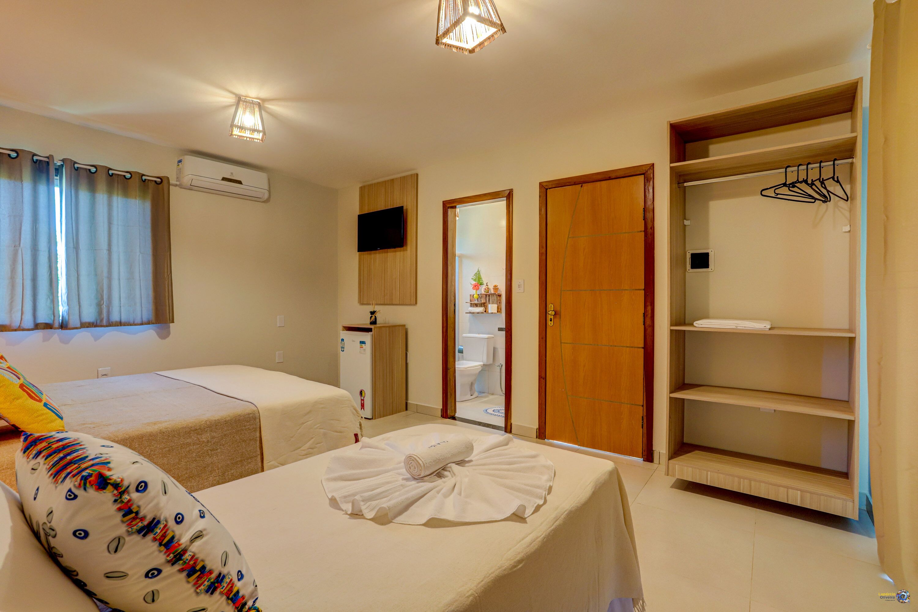 Une chambre d’hôtel avec deux lits, une armoire, un téléviseur et une salle de bain visible à travers une porte ouverte.
