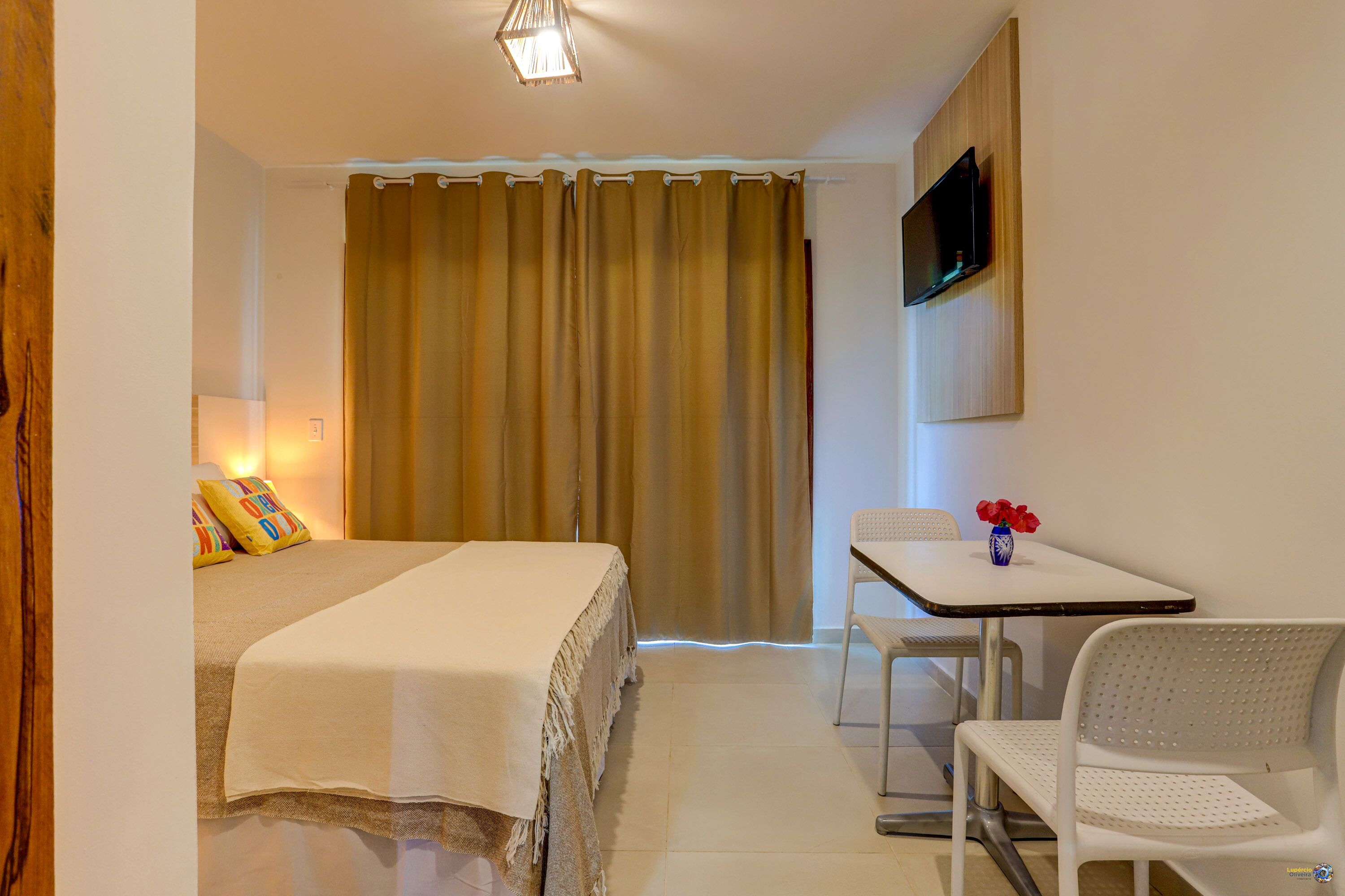 A hotel room with a bed, a desk, a chair, a TV mounted on the wall, and a curtain.