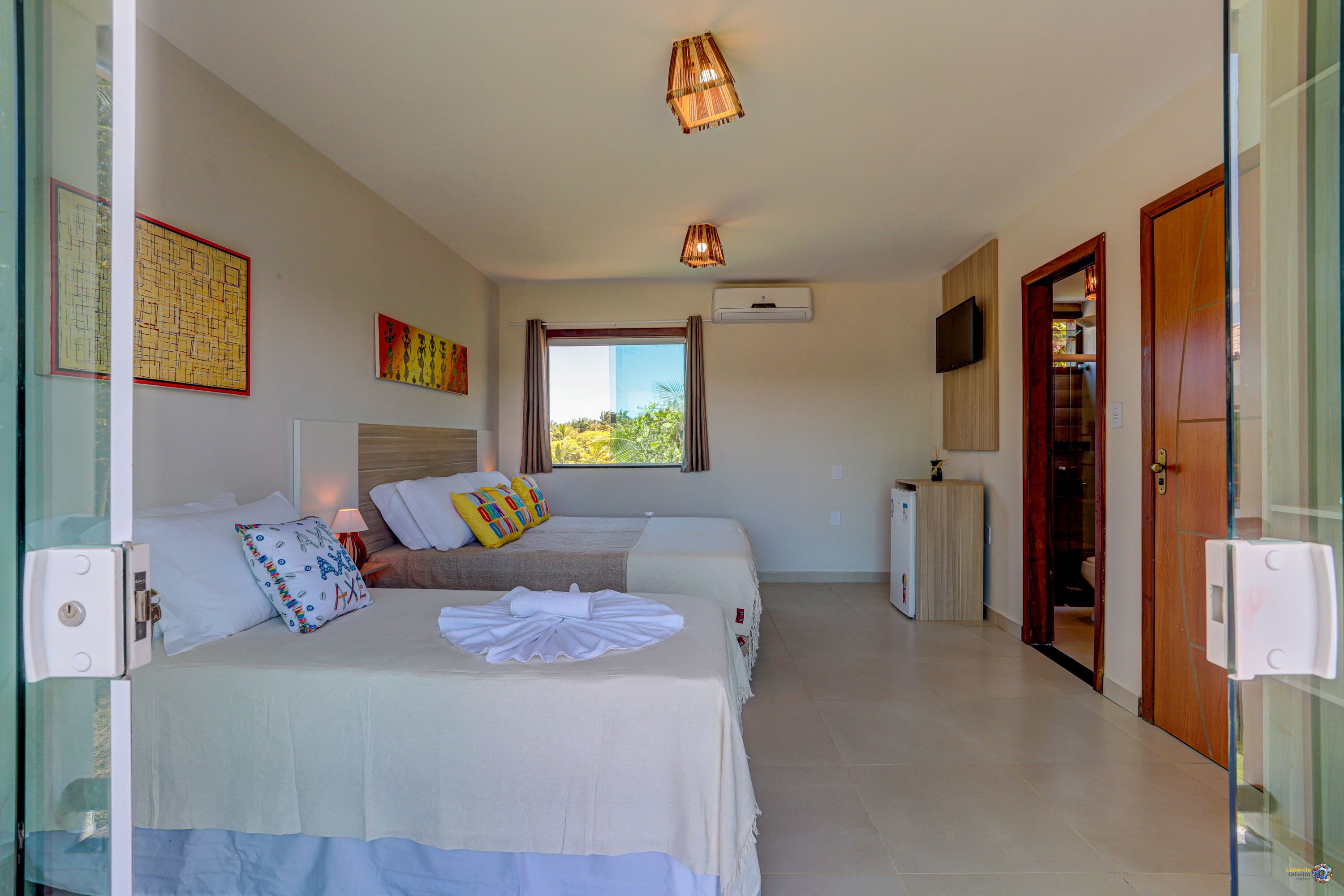 A hotel room with two beds, a TV, a window with curtains, and a door.