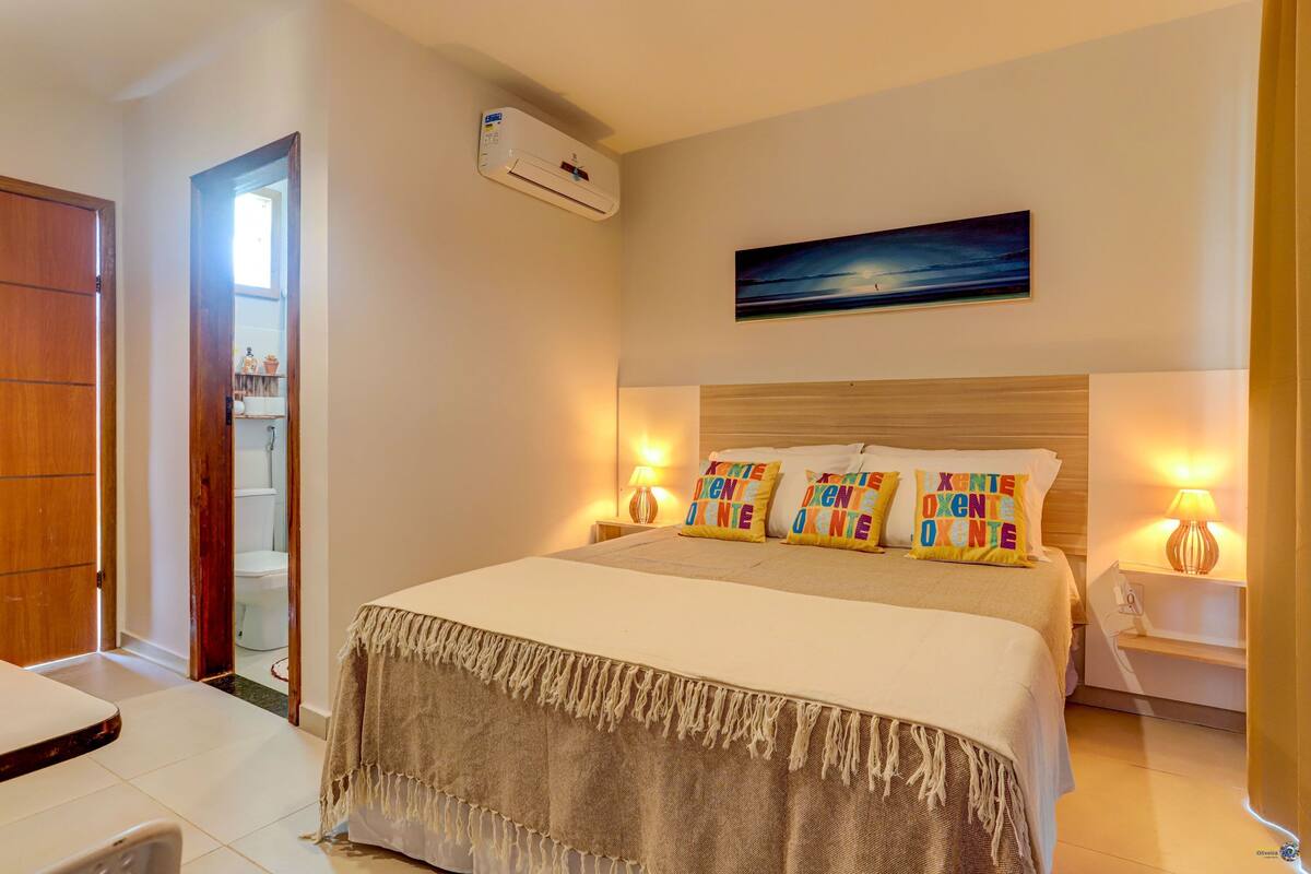 Un dormitorio con cama, lámparas de noche, mesita de noche, un cuadro y un equipo de aire acondicionado.
