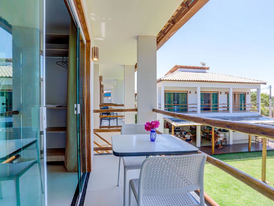 A balcony with a table and chairs, a vase with flowers, and a view of a house with a tiled roof.