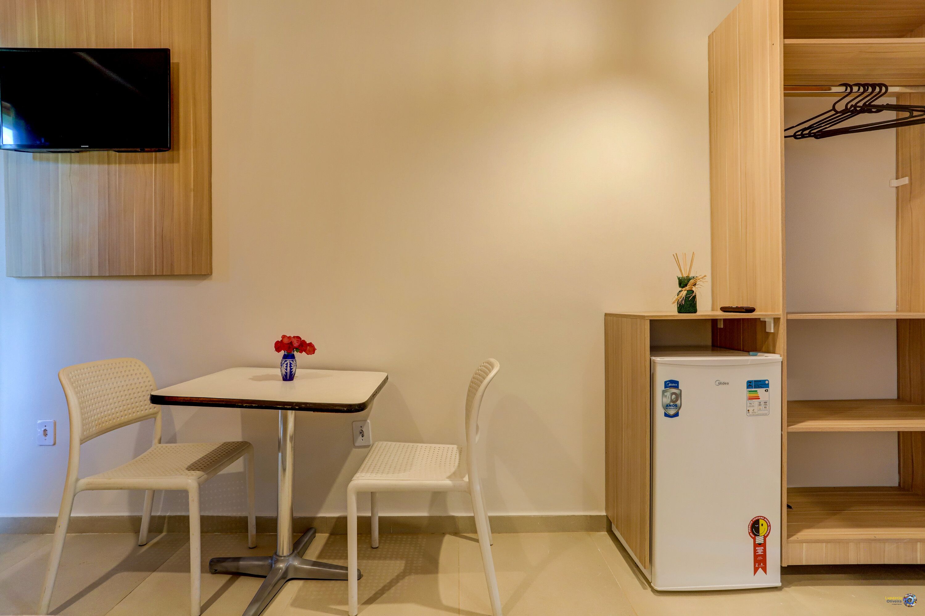 A small room with a table, two chairs, a TV mounted on the wall, and a refrigerator.
