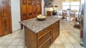 A kitchen with granite countertops, wooden cabinets, a central island with a bowl of snacks, a dining area with chairs, and a refrigerator. - Comfort and Charm Highly Recommended (Newburgh)
