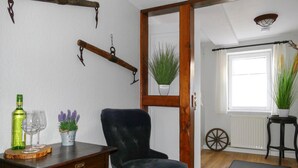 Quarto com cadeira de madeira, pequena mesa com garrafa e copos, espelho e janela com vista para o exterior.