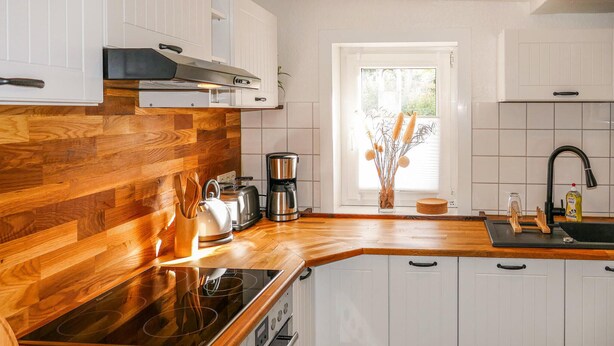 Uma cozinha moderna com armários de madeira, fogão embutido, máquina de café e janela com vista para o verde.
