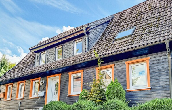 Un bâtiment à deux étages, doté d’une façade en bois sombre, de nombreuses fenêtres à encadrements orange et d’un toit recouvert de tuiles.