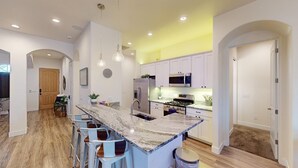 A modern kitchen with a central island, bar stools, stainless steel appliances, and a yellow accent wall. - Quiet, Cozy Three Bedroom Two Bath Home, Great Location (Page)