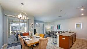 A spacious kitchen with a central island, a dining area with a wooden table and chairs, and a living area with a sofa and coffee table. - Town Home With Pool in Gated Golf Community Of Champions Gate Resort (Davenport)