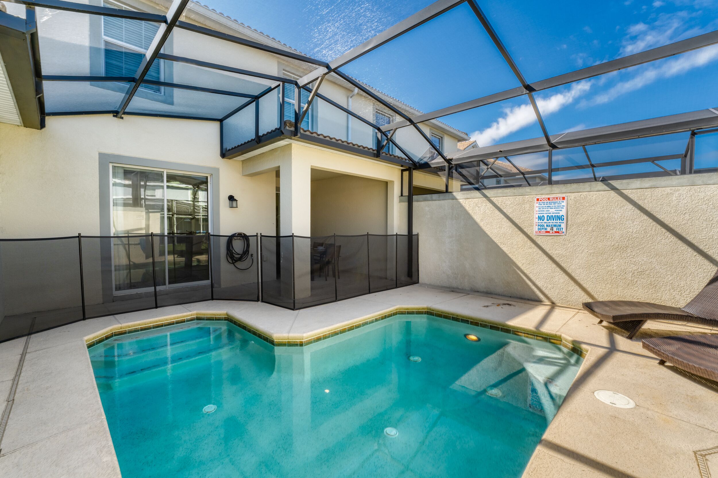 Une piscine entourée de parois en verre, un patio couvert et un panneau indiquant « Il est interdit de plonger ».