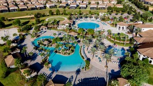 An aerial view of a resort with multiple swimming pools, palm trees, and a well-maintained lawn. - Town Home With Pool in Gated Golf Community Of Champions Gate Resort (Davenport)