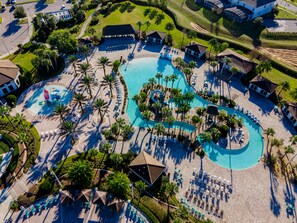 An aerial view of a resort with a large, winding pool surrounded by palm trees and sun loungers. - Town Home With Pool in Gated Golf Community Of Champions Gate Resort (Davenport)