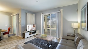 A modern living room with a sofa, a coffee table, a TV, and a sliding glass door leading to a balcony. - Town Home With Pool in Gated Golf Community Of Champions Gate Resort (Davenport)