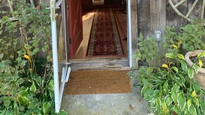 A wooden building entrance with a red door, a wooden interior visible through the doorway, and a large wooden wheel on the right wall. - Rustic two bedroom cottage on riverside in Shohola PA (Shohola)