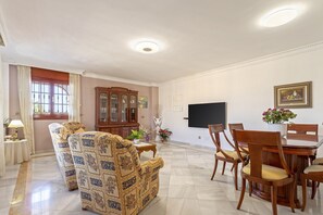 A living room with a sofa, dining table, chairs, a cabinet, and a flat-screen TV.