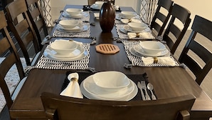 A dining table set with white plates, bowls, and cutlery, surrounded by dark wooden chairs with cushioned seats. - in Glendale Near stadium, entertainment & shopping (Glendale)